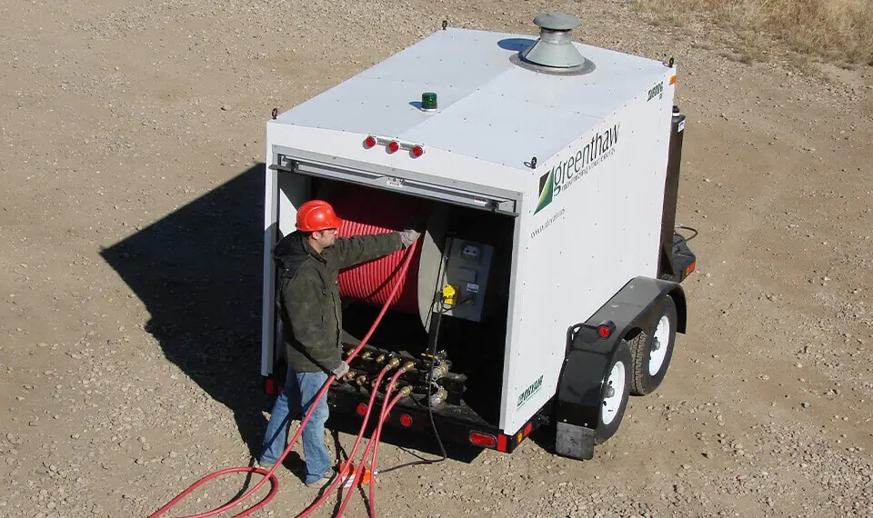 A construction worker unspooling hose from a hydronic surface heater on a job site.