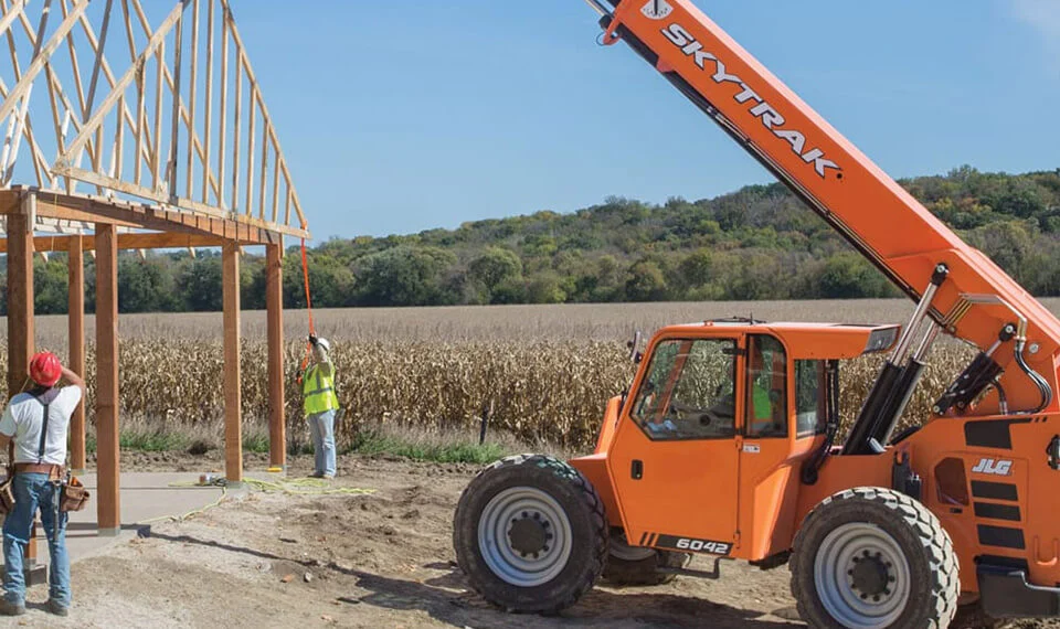 Construction workers using a reach forklift to set trusses on a new building.