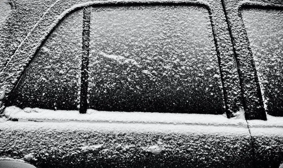 A black and white photo of a car covered with a dusting of snow.