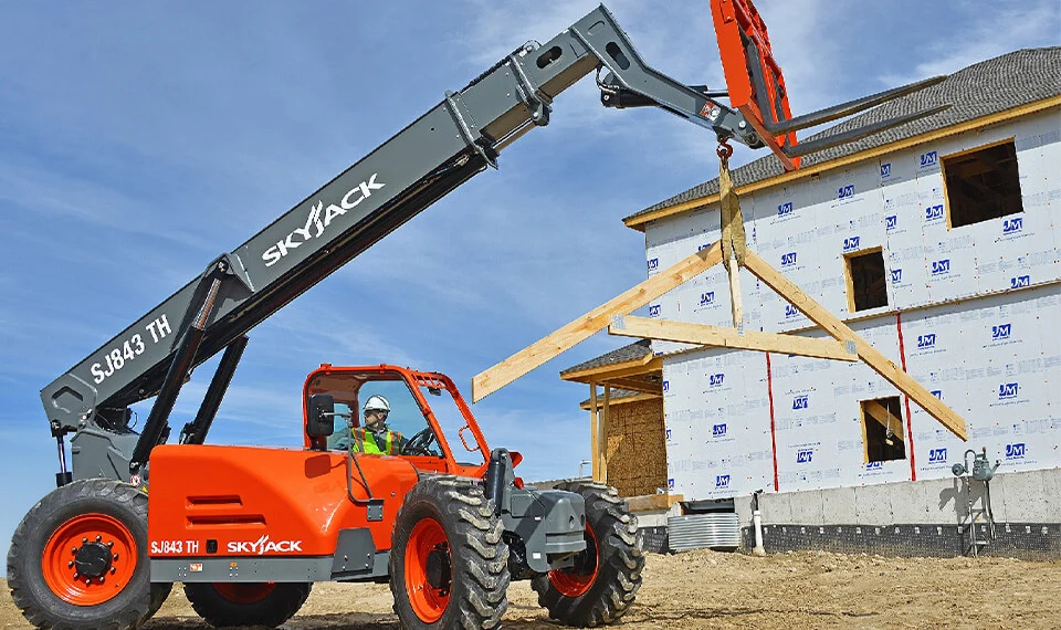 A construction worker using a rough terrain forklift at a construction site for a new home.