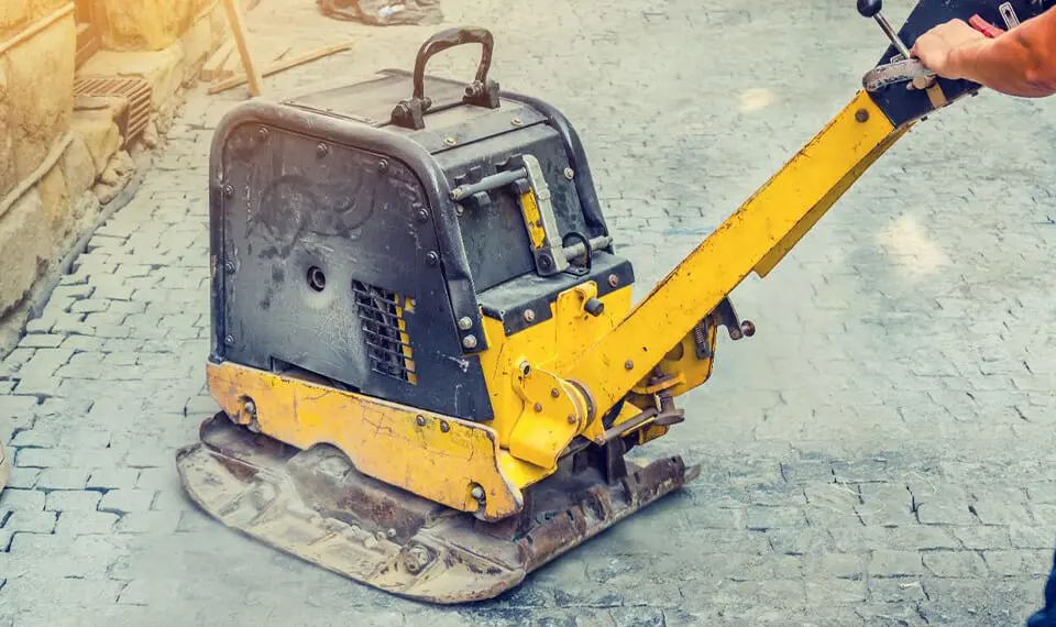 A worker using a reversible plate compactor on paving stones.