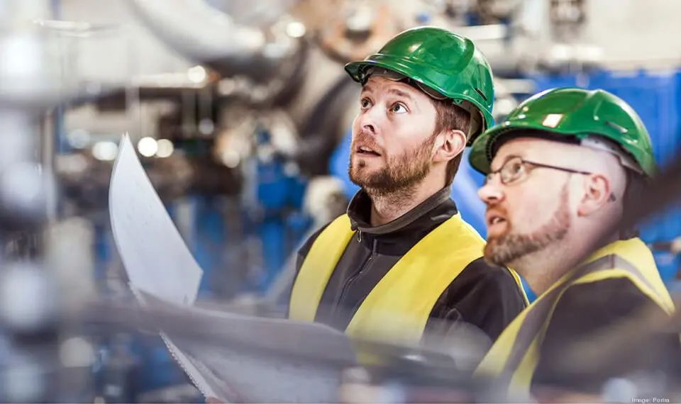 Two workers wearing hard hats and reviewing machinery.