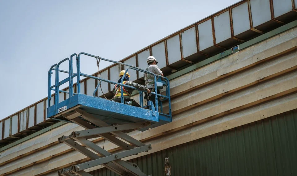 Workers using an electric scissor lift to perform work on a building.