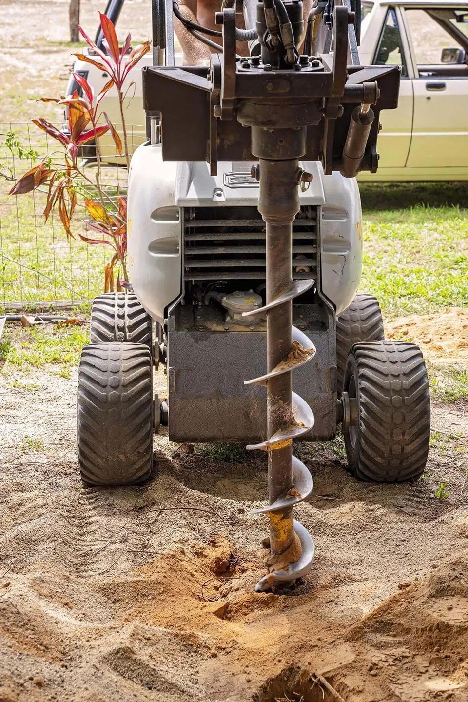 A worker using an auger to drill holes in the ground at a work site.