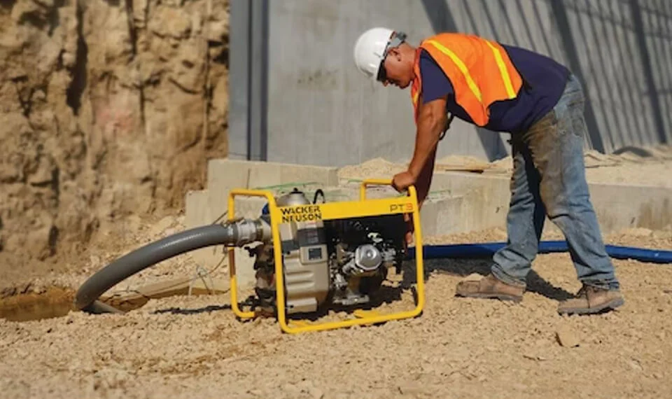 A construction worker using a trash pump at a work site.