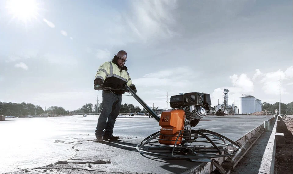 A construction worker using a power trowel on a concrete slab.