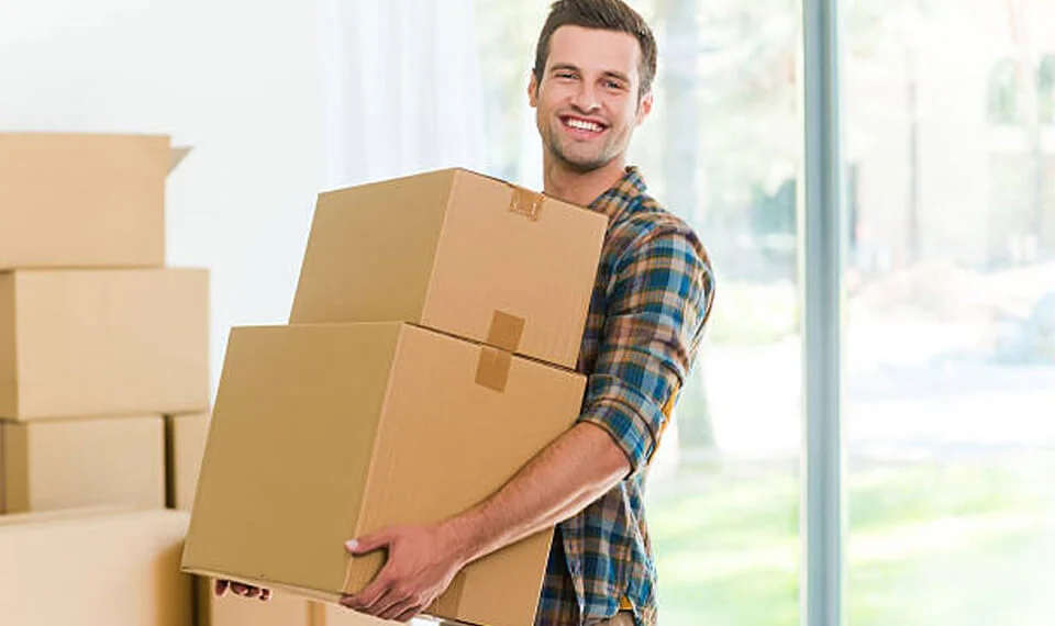 A photo of an individual carrying a stack of cardboard boxes.