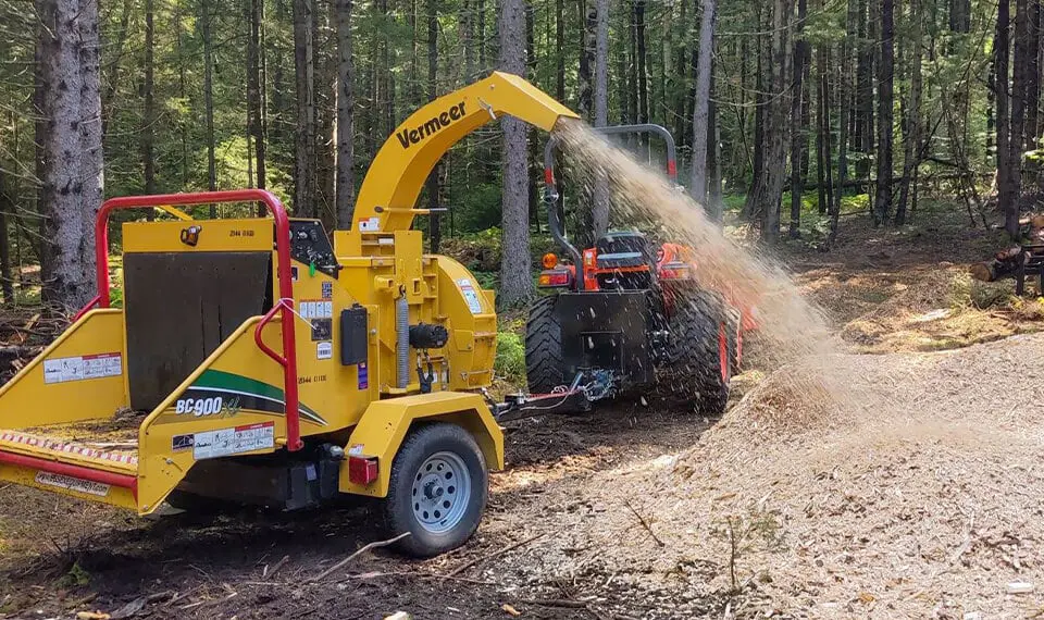 A wood chipper in use in the forest to chip up trees.