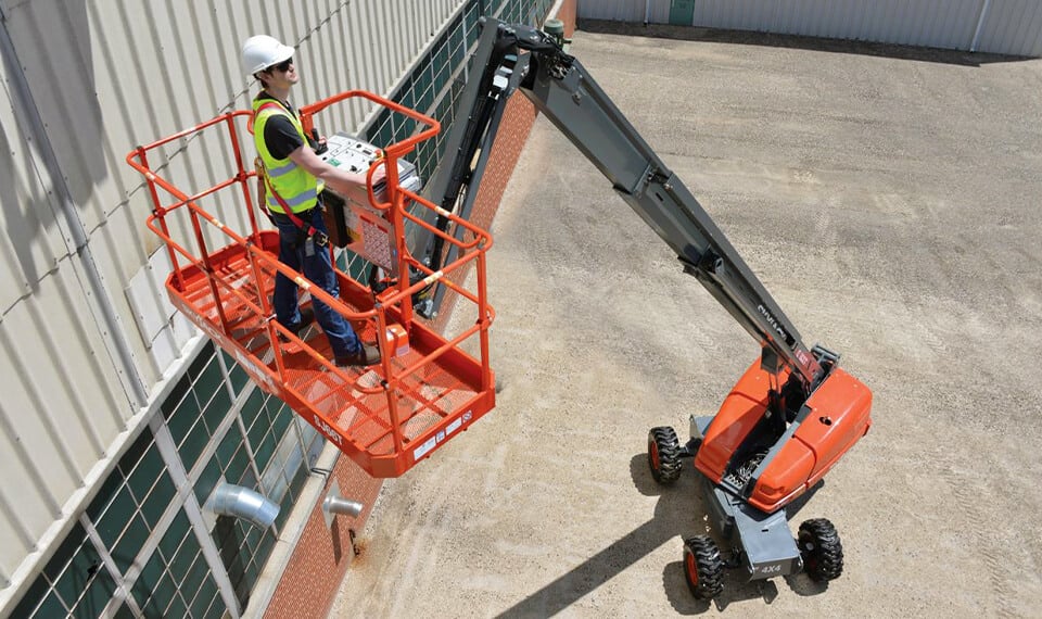 A construction worker elevated in the air on a boom lift.