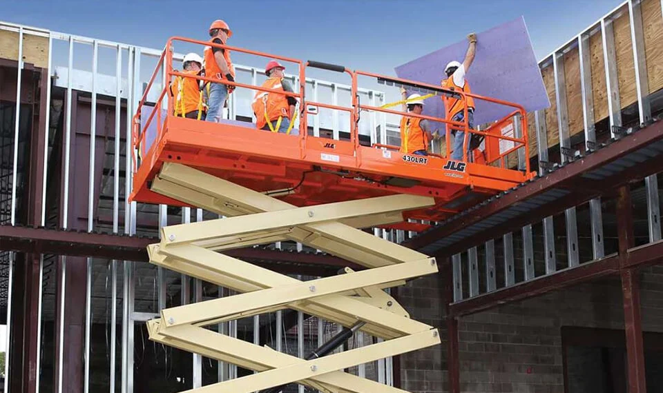 Construction workers on a job site using a scissor lift to work on a new unfinished building.