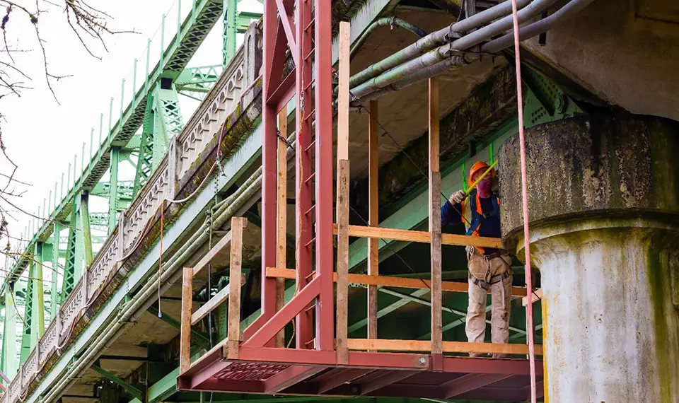 A construction worker using an under bridge inspection trailer to inspect a bridge.